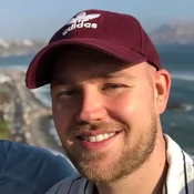 Adam smiling wearing a red adidas cap.